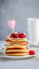 A stack of pancakes with raspberries and heart decor
