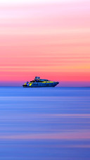 Colorful seafront sunset with yacht on horizon