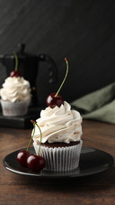 Delicious cupcake with cream and cherries on wooden table