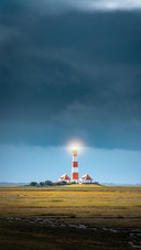 A lighthouse in the field against a cloudy sky