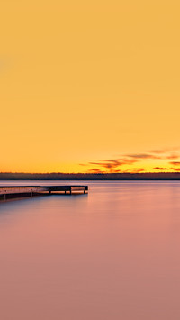 Sunset on the lake shore with a footbridge and a calm water