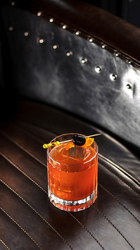 A cocktail with ice and a toothpick with olives in a glass