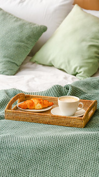 Tray with cup of coffee and croissant on bed