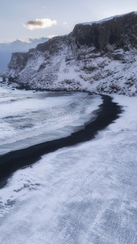 The black sandy beach like a silk ribbon after the snow