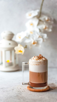 Hot latte macchiato in tall glass with foam, on table settin