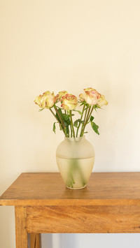 Vertical view of cream roses in glass vase on oak side table