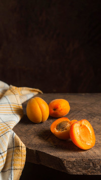 Two whole and half apricots on a vintage wooden background