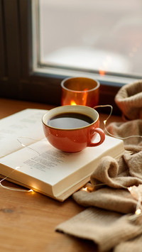 Cup of Coffee, Book, Autumn Leaves and Candle on Window
