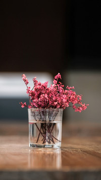 Vintage pink flowers in a glass placed on a wooden table