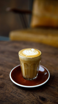 Small cup of coffee with heart pattern froth on wooden table
