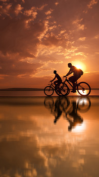 Two mountain biker silhouettes at sunrise on water