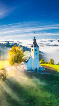 Small church on the hill in low clouds at sunrise