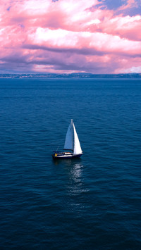 White sailboat on blue water against the coastline