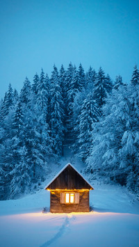 Fantastic winter landscape with glowing wooden cabin in snow