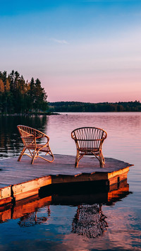 Two wooden chairs on a wood pier overlooking a lake