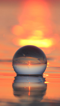 Transparent globe in shallow sea reflecting sunset