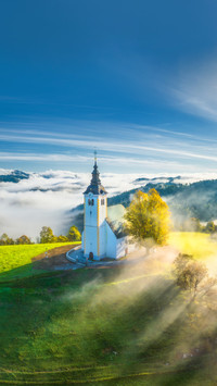 View of small church on the hill in low clouds at sunrise