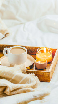 Tray of coffee and candles with warm plaid on white bedding
