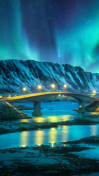 Bridge and northern lights over snowy mountains