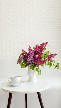A cup of tea on a table with a bouquet of purple lilacs