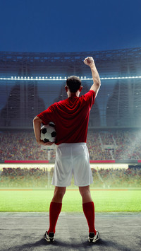 A male soccer player in red jersey standing with ball