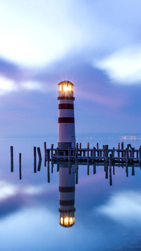 A lighthouse reflected in a lake during colorful sunset
