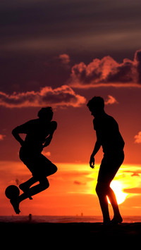 Silhouette of two teenagers playing soccer in the sunset
