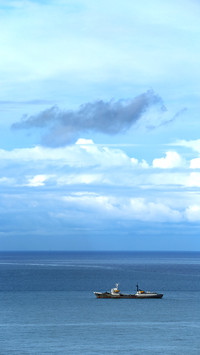 A cargo ship sails under a cloudy sky