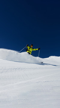 Alpine skier skiing downhill, blue sky on background