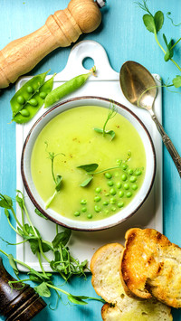 Light summer green pea cream soup in bowl with sprouts