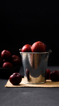 Red plum fruit in a bucket on black background