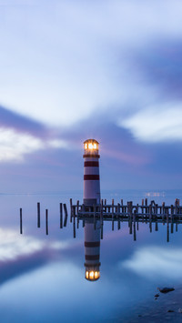 A lighthouse reflected in a lake during colorful sunset