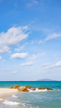 Clean beach and stones extending into body of blue sea