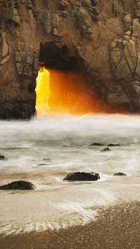 Sun setting through arch in rock at pfeiffer beach
