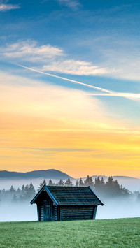 Mountain meadow with small hut with light ground fog