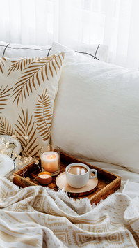 Wooden tray of coffee and candles on bed