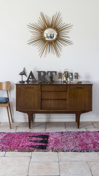 Exotic wood sideboard below sunburst mirror and various