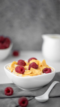 Cornflakes with milk and raspberries on a white table