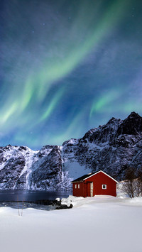 Northern Lights over a frozen lake and red rorbu, Norway