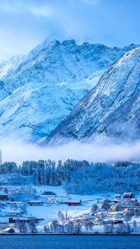 Snowy mountain with houses by the river with low clouds