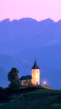 A hilltop church at sunset, framed by mountain ranges