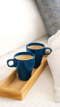 Wooden tray with cups of coffee near soft blanket on bed