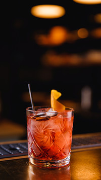A bright orange cocktail in a transparent glass with ice
