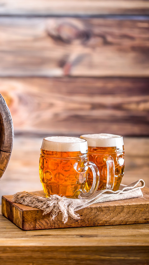 Two glasses full of beer with wooden barel preview