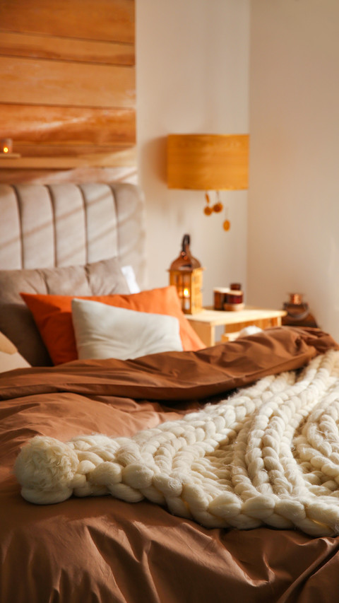 Bed with cozy knitted blanket and cushions indoors preview