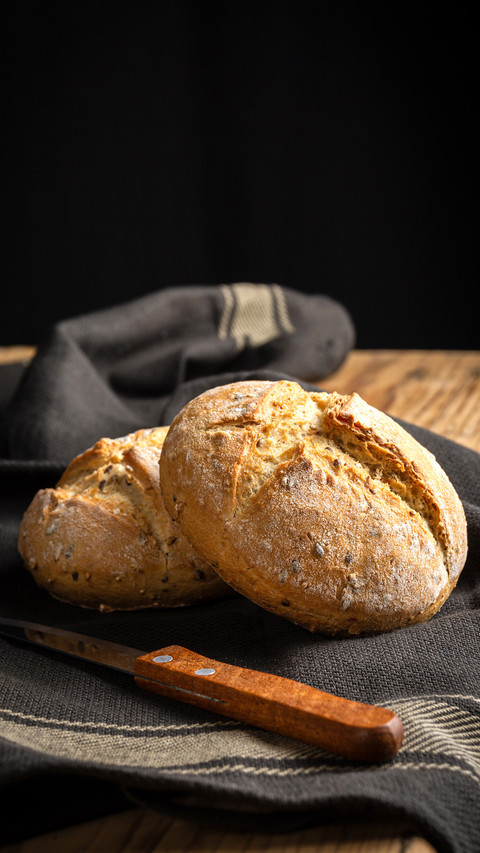 Two quinoa breads on dark cloth with knife on wooden table preview