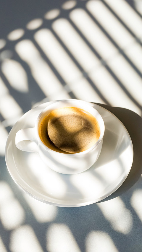 White cup of coffee in sunlight and shadows from above preview