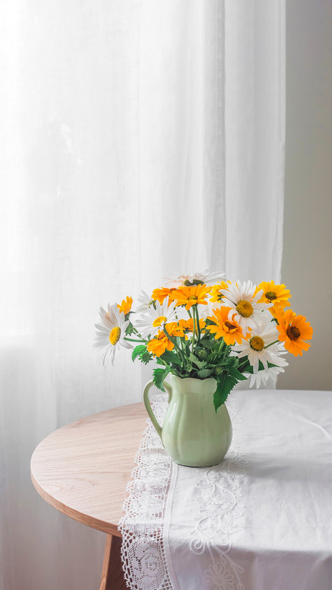 Garden daisies in a ceramic jug on a round wooden table preview